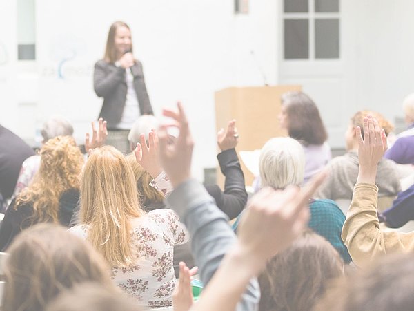 Abbildung einer Kongresssituation mit Publikum und einer Rednerin